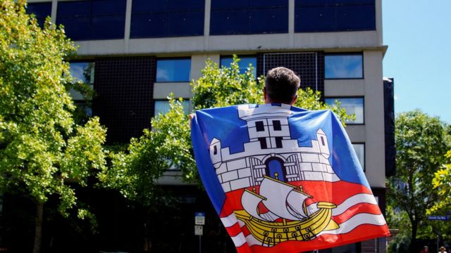 A fan draped in a Serbian flag in front of the Park Hotel in Melbourne, where Novak Djokovic is reported to be temporarily detained