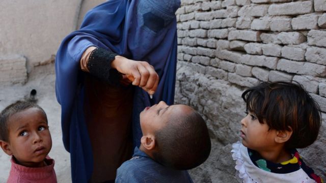 Una mujer en Afganistán con un atuendo tradicional, burka, que cubre su rostro, pone gotitas de la vacuna oral de polio en la boca de un niño.