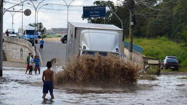 Menino observa caminhão passando por enchente próximo à ponte da Vila Any