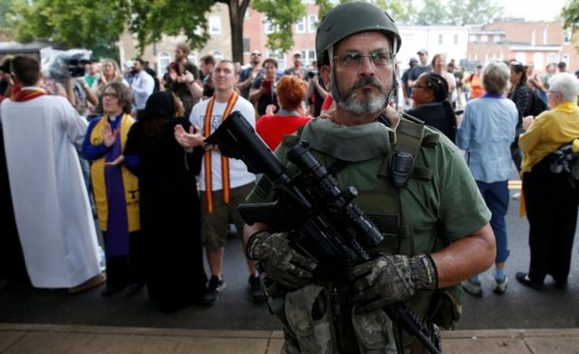 Представитель "ополчения" националистов стоит на фоне религиозного собрания, протестующего против марша.