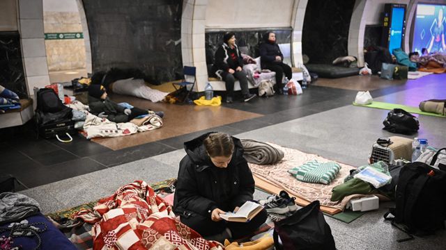 A woman reads a book as she sits in an underground metro station used as bomb shelter in Kyiv on March 2, 2022