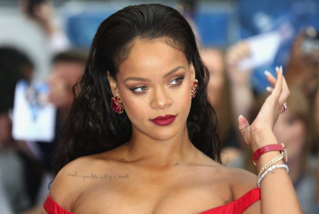 Close up of Rihanna at a gala, wearing a red dress and red accessories and jewelery
