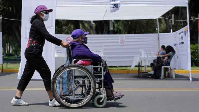Una mujer acompaña a otra en silla de ruedas para votar en Perú