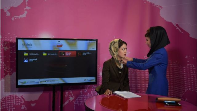 Uma mulher afegã ajusta o lenço de cabeça de um apresentador antes de gravar na estação Zan TV (TV Feminina) em Cabul (24 de maio de 2017)