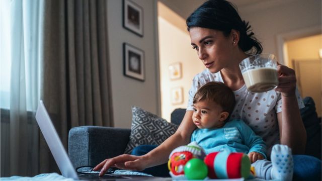 A woman working from home with a baby sitting between her and her computer