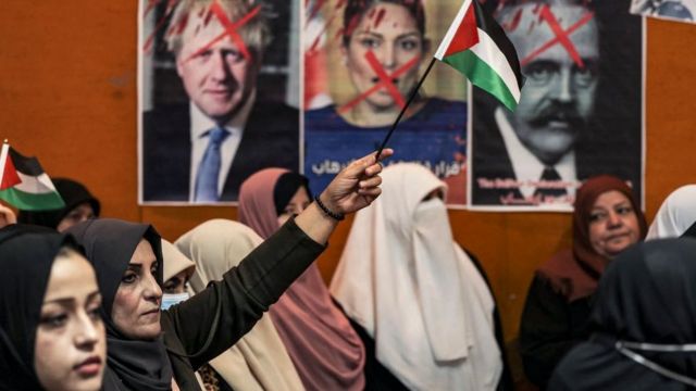 إمرأة تجلس وخلفية صور تعبر عن التنديد بقرار بريطانيا اعتزامها تصنيف حركة حماس منظمة إرهابية