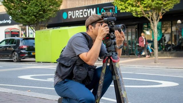 阿军在英国拍摄时仍然穿着当初在直播拍摄香港反修例示威时穿着的摄影背心。(photo:BBC)