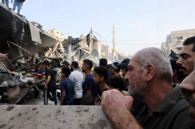Palestinos em meio a ruínas de edifício destruído por ataque aéreo israelense na noite de sexta-feira, 27 de outubro, no norte de Gaza