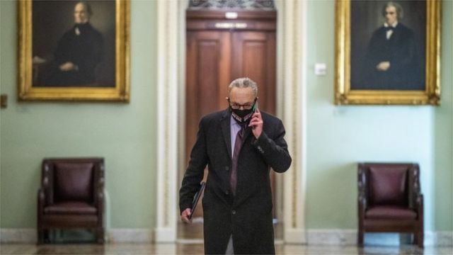 Schumer, um homem idoso de cabelo branco e crespo, fala ao telefone usando máscara