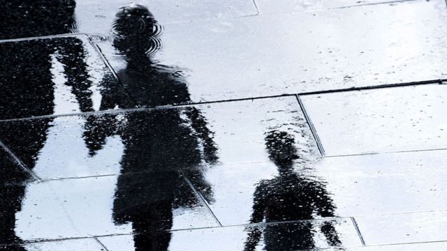 Reflexo em poça de mãe caminhando na chuva com o filho