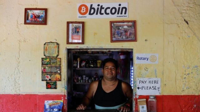 Salvadorenho em uma loja com cartaz de bitcoin