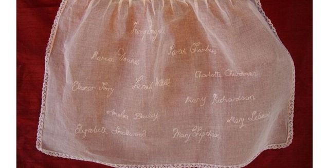 Nomes das crianças bordados em um avental infantil por uma voluntária da comunidade local