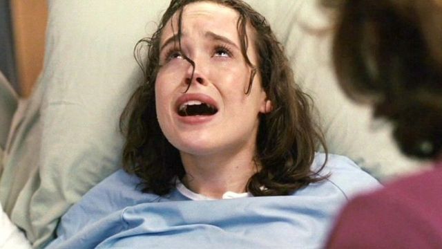 A atriz Ellen Page, semi sentada em uma cama, faz cara de dor