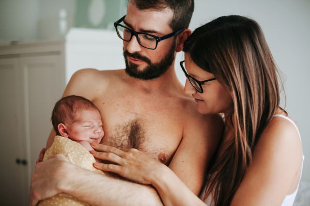 Una pareja sostiene a su bebé y todos están medio desnudos.