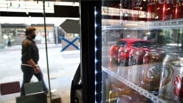 A man passes a store with canned drinks as cola