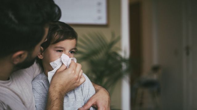 Pai com filho no colo assoando seu nariz