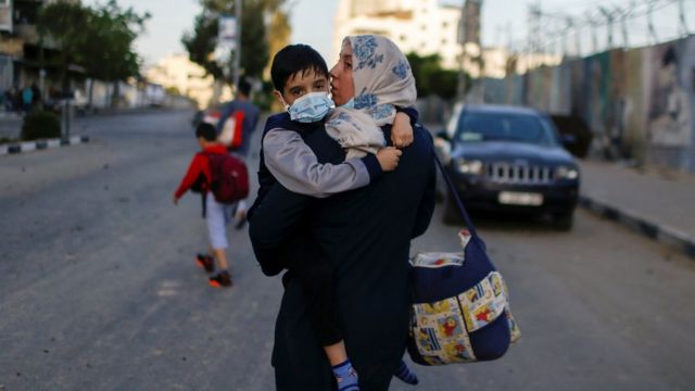 A Palestinian woman carries her son after their apartment building was hit in an Israeli air strike in Gaza City (12 May 2021)