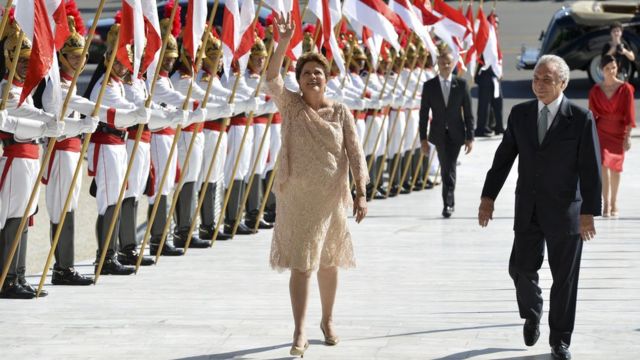 Dilma Rousseff e Michel Temer sorriem caminhando em corredor formado por dragões (guardas)