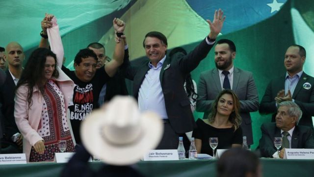 Em pé, Paschoal e Bolsonaro aparecem sorrindo durante evento que oficializou o nome dele na eleição de 2018, da qual saiu vencedor, em meio a outros correligionários