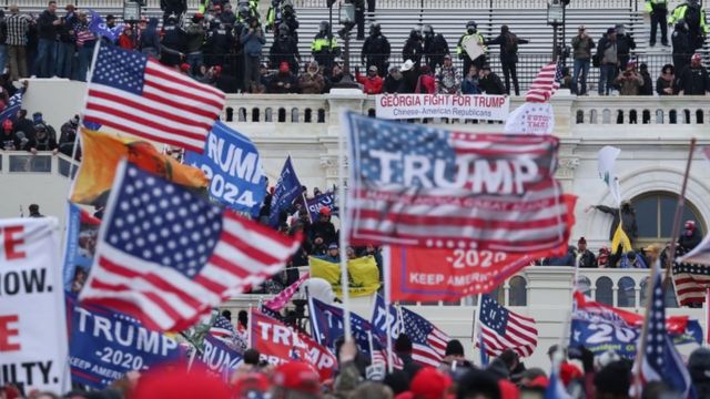 Multidão com bandeiras dos EUA e com nome de Trump em frente ao prédio do Capitólio