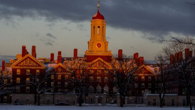 Fotografia colorida mostra o prédio de uma das faculdades da Universidade de Harvard sob um céu de nuvens escuras