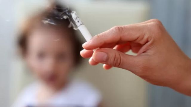 A hand holding a lit cigarette in front of a child