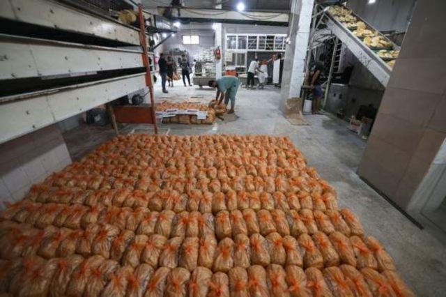 Funcionários de padaria preparam pacotes de pão para pessoas que se aglomeram em Rafah