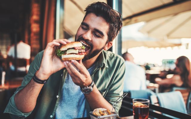 Homem jovem mordendo hambúrguer em restaurante