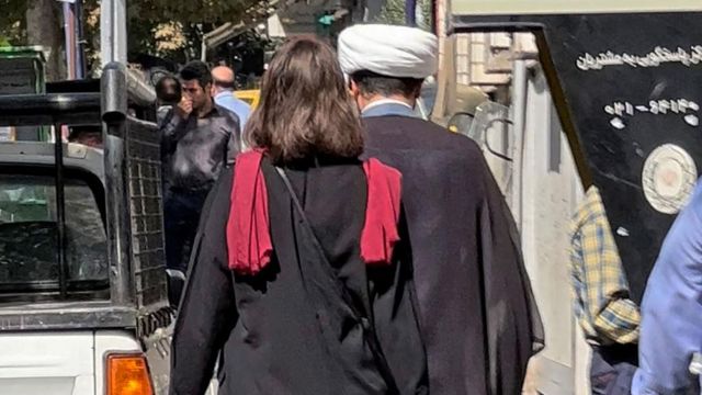 زنی بدون حجاب پشت مردی معمم در خیابانی در تهران راه می‌رود