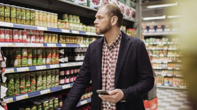 Homem no corredor de supermercado com celular na mão