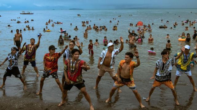 Imagem mostra filipinos dançando na praia, no fundo várias pessoas tomam banho