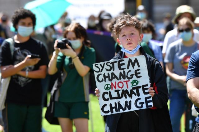 Menino com um cartaz que pede mudança no sistema em vez de mudança climática