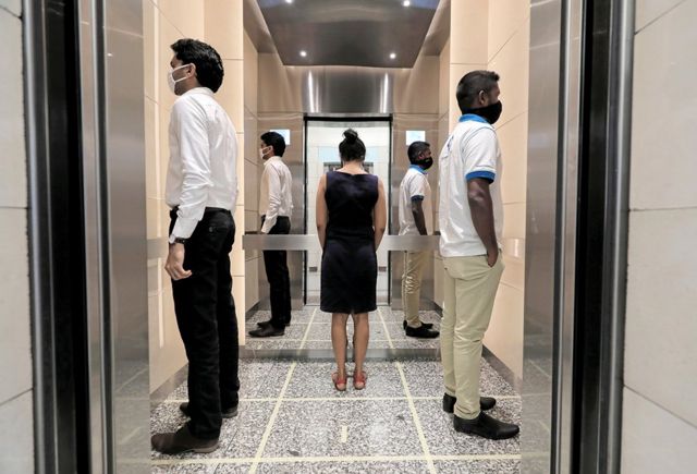 People stand in an elevator wearing face masks with their backs to each other