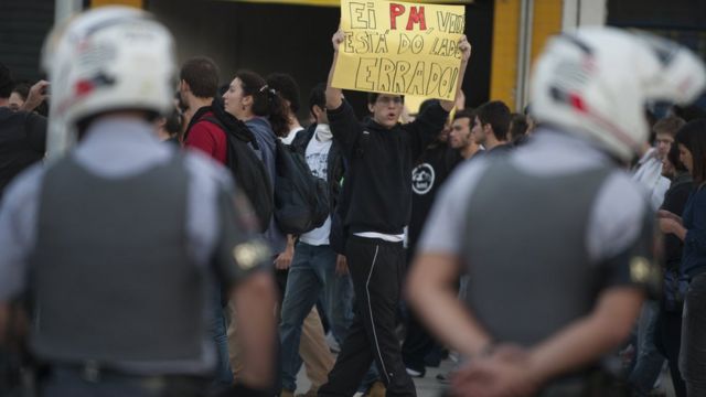 Manifestante com cartaz para a polícia, perto de policiais, em junho de 2016