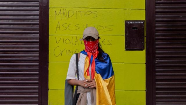 Una manifestante con el rostro cubierto frente a un muro con un grafiti que lee: "Malditos, asesinos, violadores, ciminales", en Medellín, 19 de mayo de 2021