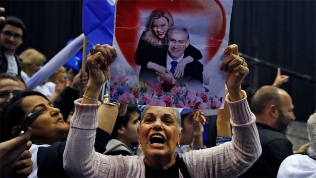Seorang pendukung partai Likud mengangkat poster yang menunjukkan Perdana Menteri Benjamin Netanyahu dan istrinya, Sara.