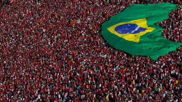 Multidão vestida de vermelho em posse de Lula carregando bandeira do Brasil