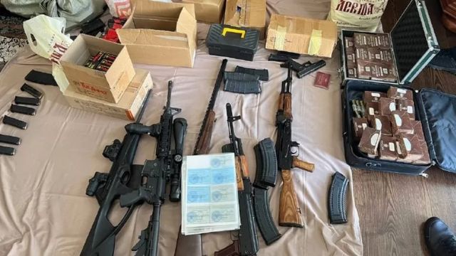  um grande estoque de armas - incluindo rifles de assalto, pistolas e munições - sobre uma cama.