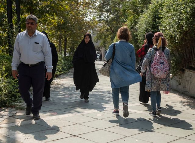 یک زن چادری زیر چشمی به دو دختر که در تهران حجابشان را برداشته‌اند نگاه می‌کند