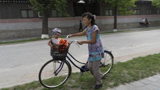 A mother watches her child, who sits in the basket of a bicycle