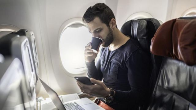 Homem com celular e laptop em avião