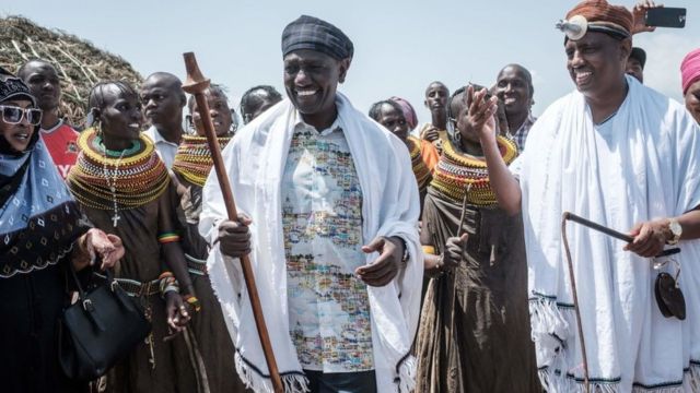 William Ruto et le gouverneur du comté de Marsabit Mohammed Muhamud Ali marchent avec des artistes de la tribu Turkana lors du 11e festival culturel du lac Turkana de Marsabit à Loiyangalani près du lac Turkana, dans le nord du Kenya, le 28 juin 2018.