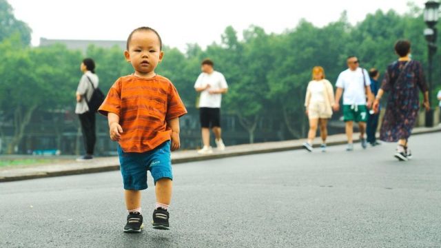 Um menino de camiseta laranja olha para a câmera