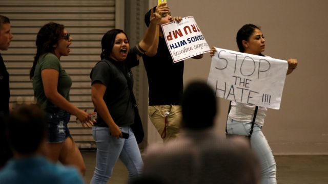 支持者集会の会場外で「憎むのを止めて！」などとトランプ氏に抗議する人たち（24日）