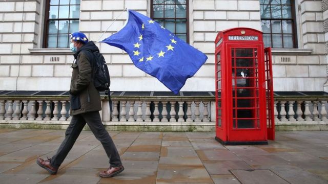 Passoa carrega bandeira da União Europeia enquanto passa em frente a uma típica cabine telefônica vermelha de Londres