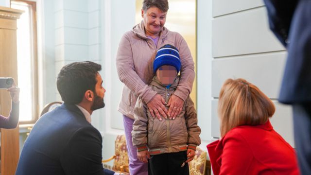 Woman embracing boy, talking to two kneeling officials