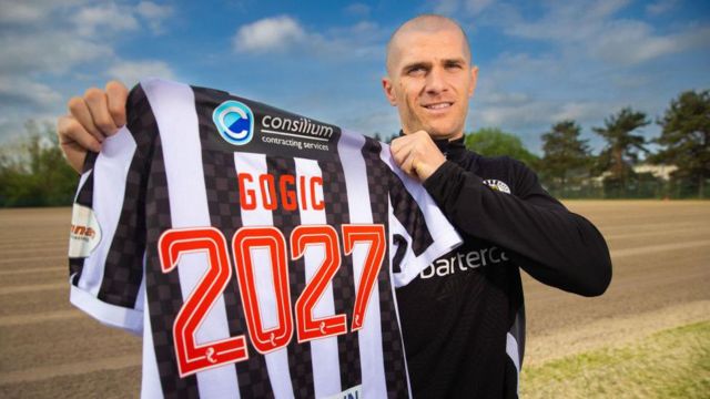 Alex Gogic holds up a St Mirren shirt with 'Gogic 2027' on the back