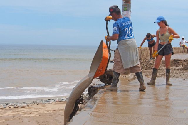 Un hombre y dos mujeres trabajan con una carretilla y rastrillos en la playa peruana de Punta Hermosa, a la que el ciclón Yaku trajo fuertes lluvias