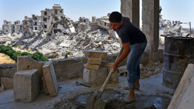 Trabalhador segura pá e trabalha em reconstrução de área da cidade de Aleppo