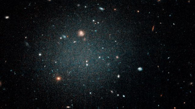 観察された銀河は非常にぼんやりとしており、その奥にある他の渦巻銀河が見えるほどだ（ハッブル望遠鏡での撮影）